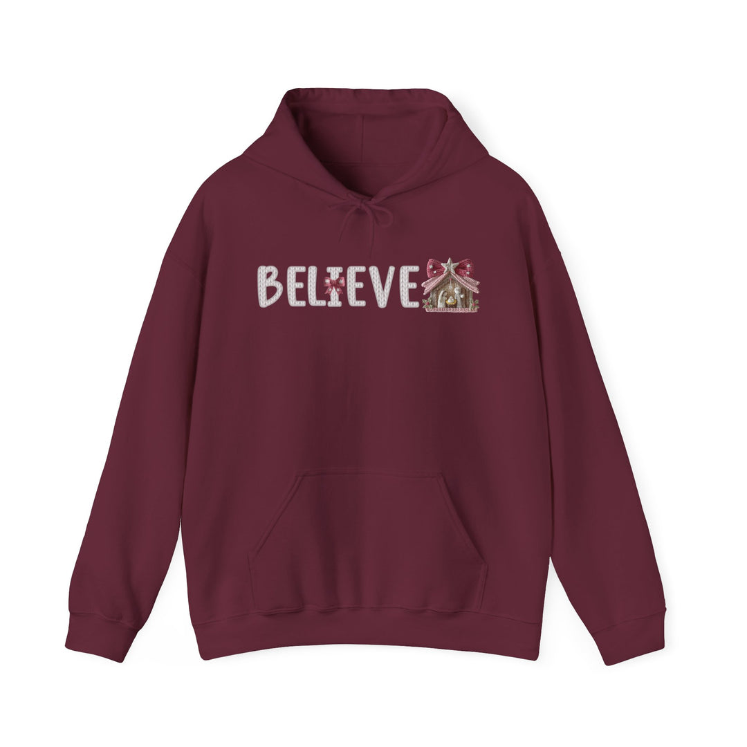 Burgundy hoodie with BELIEVE text and nativity stable design, offering warmth and style for Christmas. Perfect for cozy, festive wear.