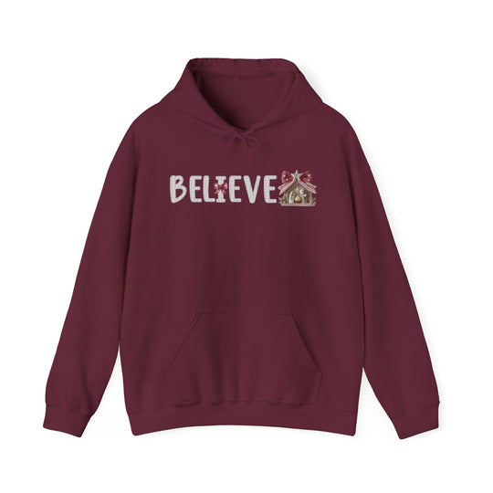 Burgundy hoodie with BELIEVE text and nativity stable design, offering warmth and style for Christmas. Perfect for cozy, festive wear.
