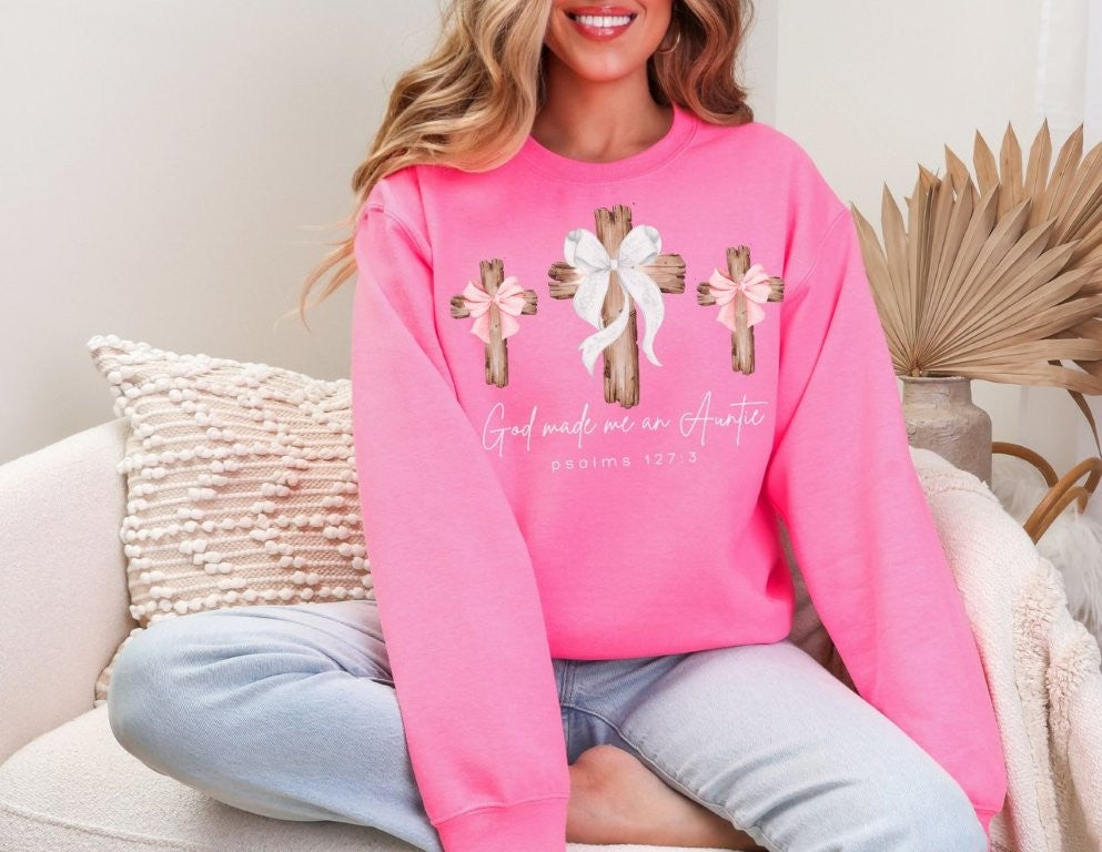 Person on sofa wearing God Made Me an Auntie sweatshirt with wooden crosses design, showcasing Faith Family Designs' blend of comfort and style.