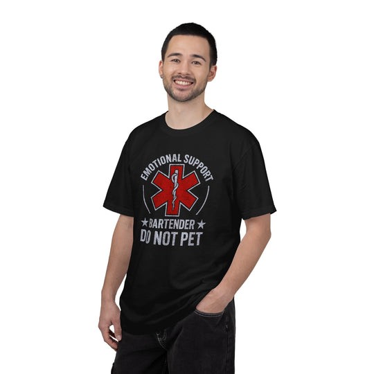 Casually dressed man wearing the EMOTIONAL SUPPORT BARTENDER TEE- 2 with a red symbol and humorous text, smiling with one hand in his pocket.