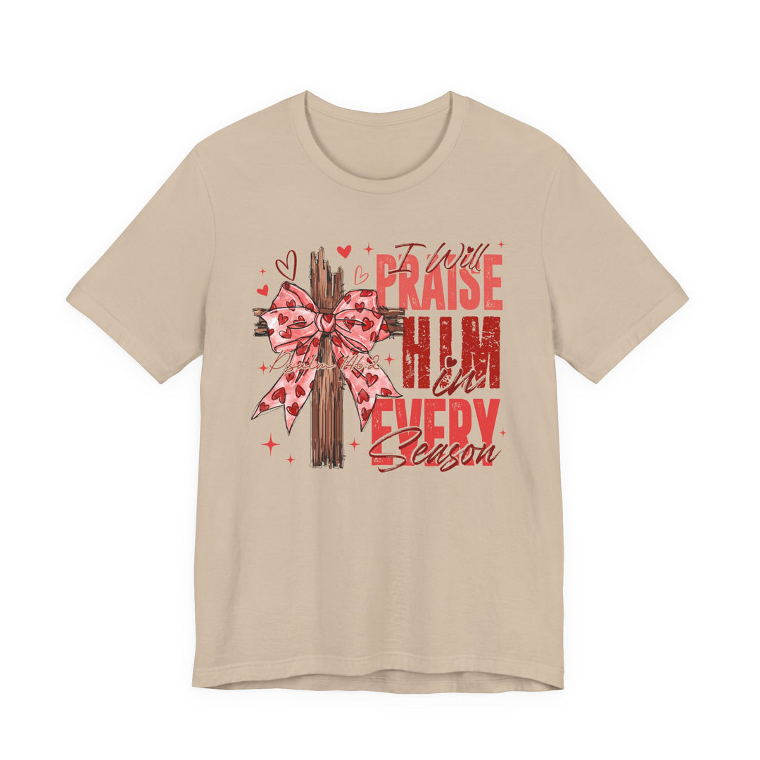 Praise in Every Season Heart Tee features a wooden cross with a pink heart-patterned ribbon, surrounded by doodles and Psalm 146:2 script on a beige T-shirt.