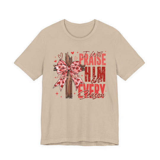 Praise in Every Season Heart Tee features a wooden cross with a pink heart-patterned ribbon, surrounded by doodles and Psalm 146:2 script on a beige T-shirt.