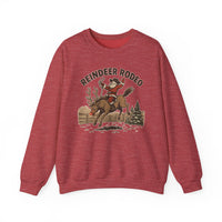 Red crewneck sweatshirt featuring a vintage-style Reindeer Rodeo graphic with Santa in cowboy gear on a bucking reindeer, set in a snowy corral.