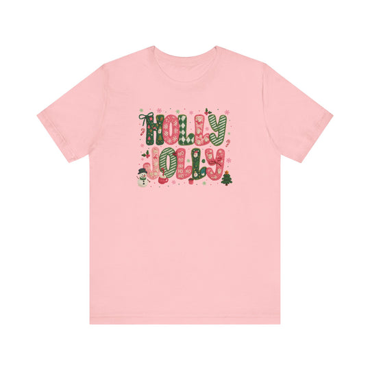 Holly Jolly Tee: Pale-pink short-sleeve shirt featuring festive HOLLY JOLLY graphic with candy-cane letters, snowman, mittens, and Christmas motifs. Classic unisex fit.