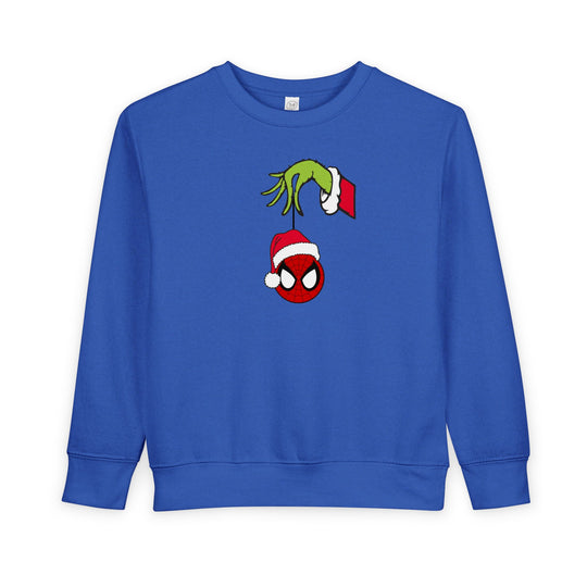 Spider Ball Christmas Toddler Crew: Blue sweatshirt with Grinch hand holding Spider-Man ornament, Santa hat. Soft, durable, CPSIA compliant for toddler warmth and style.