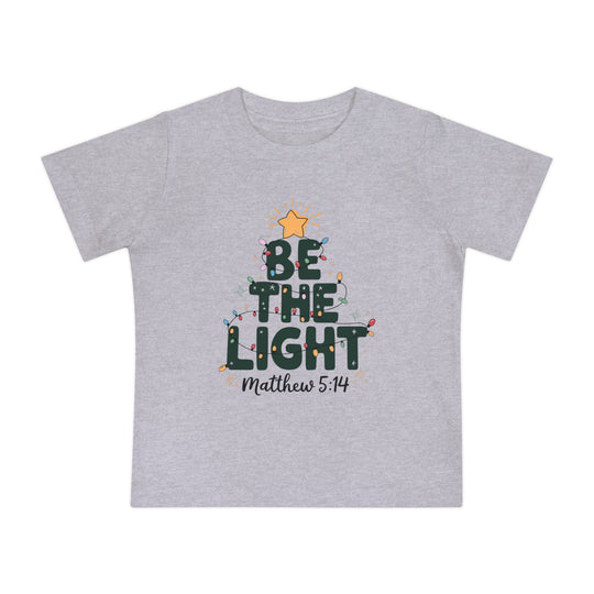 Light-gray baby tee with BE THE LIGHT in dark green, adorned with Christmas lights and sparkle accents; features Matthew 5:14 below.