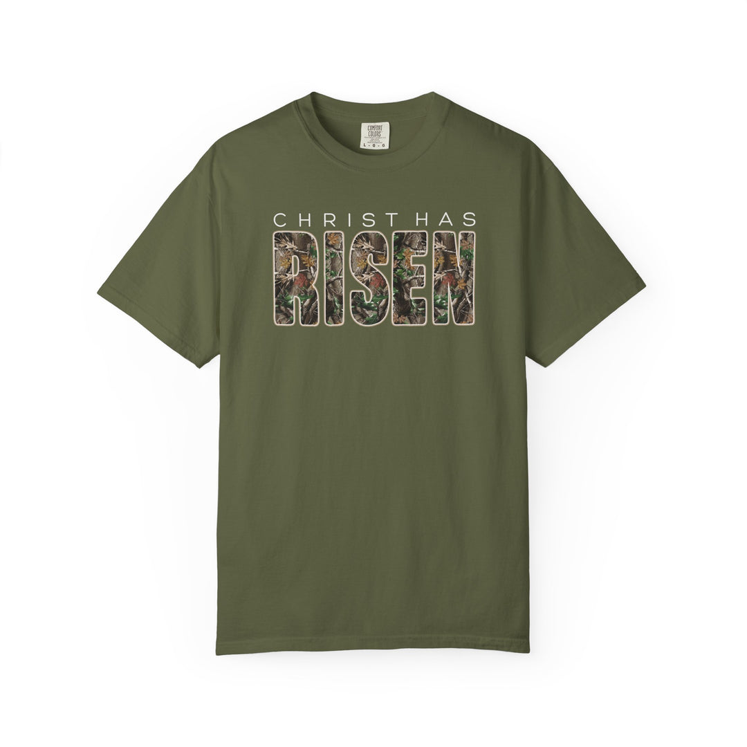 Christ has Risen Tee features an olive-green design with CHRIST HAS in white and RISEN in camo pattern, offering relaxed fit and comfort.