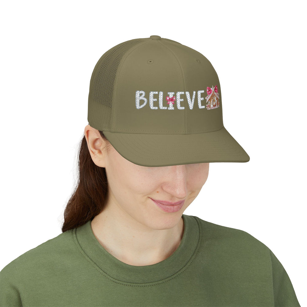Model wearing the Believe Snapback Trucker Cap, featuring a sparkly script with pink bows and gingerbread icon, paired with a green top.