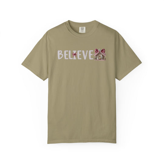 Believe Tee: Unisex crew-neck T-shirt with BELIEVE knit-style design, featuring a gingerbread house motif and red bow accent, offering relaxed fit and cozy comfort.