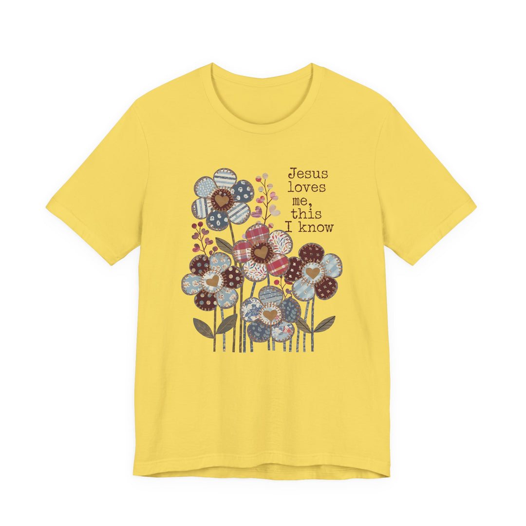 Jesus Loves Me Tee with patchwork-pattern flowers in blues, reds, browns. Soft cotton, unisex fit, ribbed collar, dual side seams.