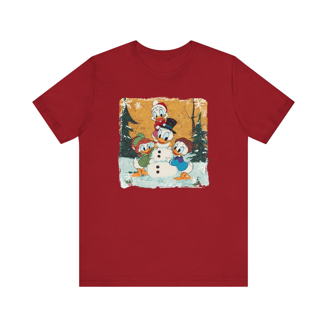 Duck Snowmen Tee features Donald Duck and nephews building a snowman in a snowy scene, capturing holiday charm. Soft, unisex fit with durable cotton.