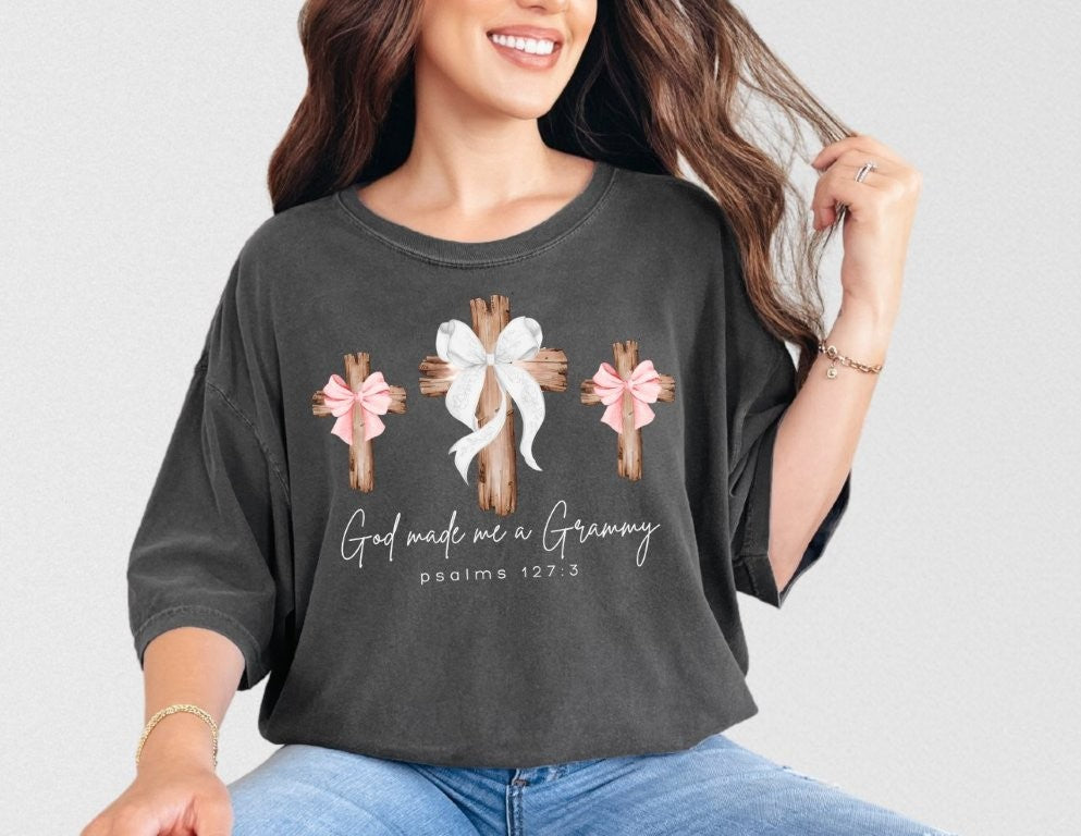 Woman wearing God Made Me a Grammy tee with three rustic wooden crosses, featuring bows, on soft, washed-black fabric by Faith Family Designs.