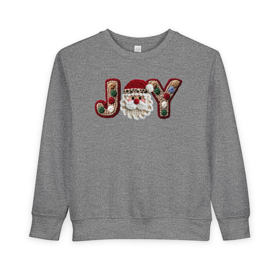 Joy Toddler Crew sweatshirt featuring a festive JOY graphic with a smiling Santa face, tufted yarn letters, and pom-pom accents, perfect for holiday warmth.