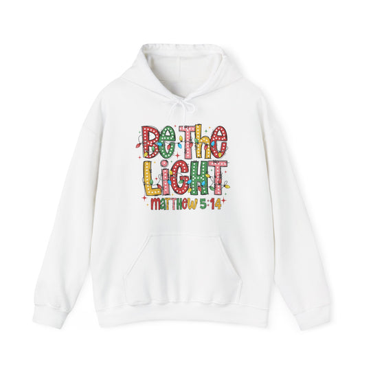 White pullover hoodie featuring Be the Light in colorful letters with Christmas lights and Matthew 5:14 below, kangaroo pocket, and drawstring hood.