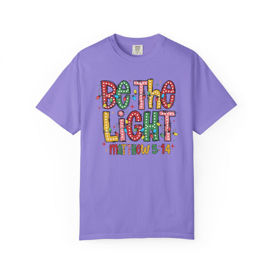 Be the Light Tee featuring festive bulb design and Matthew 5:14 reference on lavender crew-neck, offering relaxed fit in various sizes, ideal for Faith Family Designs.