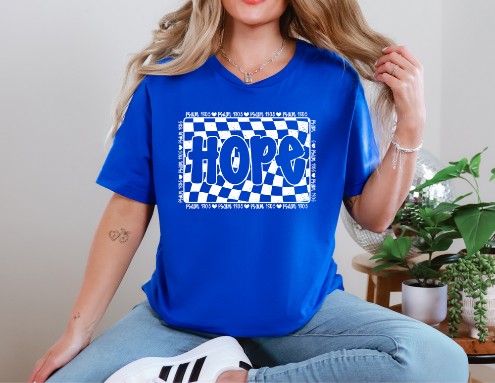 Woman wearing the Hope Tee, a classic unisex jersey short sleeve tee, sitting on a chair. The tee features soft cotton and ribbed knit collars for comfort.