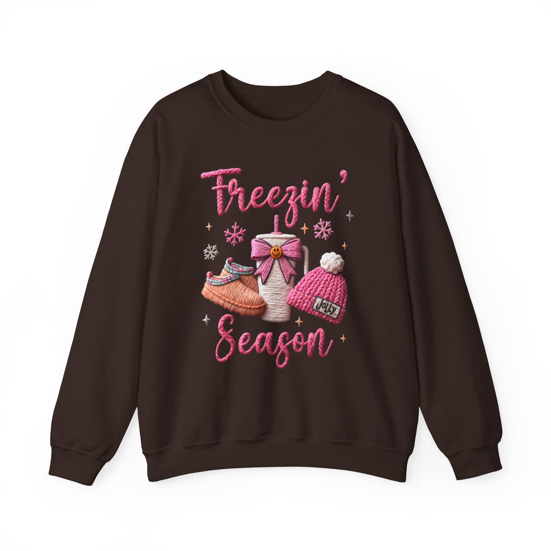Freezin Season Crew sweatshirt features cozy winter graphics, including a steaming mug, fuzzy slippers, and 'Jolly' beanie, perfect for chilly weather comfort.