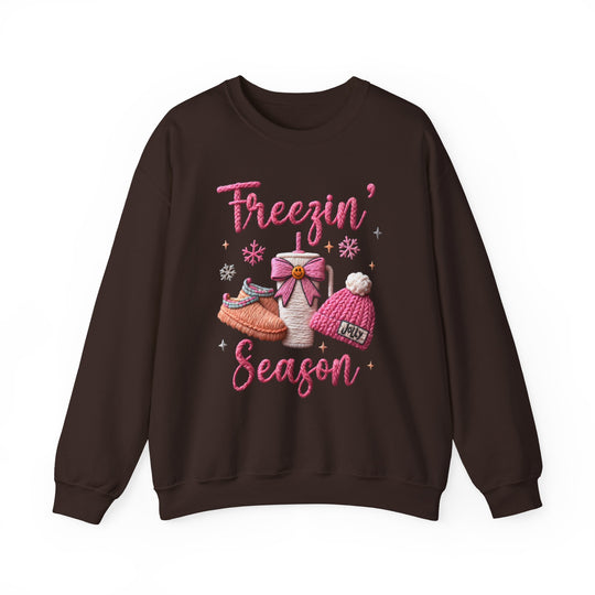 Freezin Season Crew sweatshirt features cozy winter graphics, including a steaming mug, fuzzy slippers, and 'Jolly' beanie, perfect for chilly weather comfort.