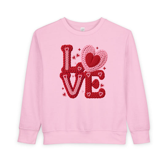 Light-pink toddler crewneck sweatshirt featuring a stylized LOVE graphic in chunky knit yarn design with nested hearts, perfect for warmth and durability.