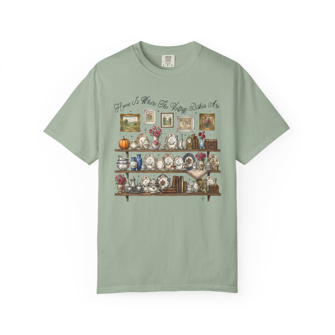 Vintage Dishes Tee featuring a cozy vintage illustration of shelves with antique china and decor, complemented by the phrase “Home Is Where The Vintage Dishes Are.”