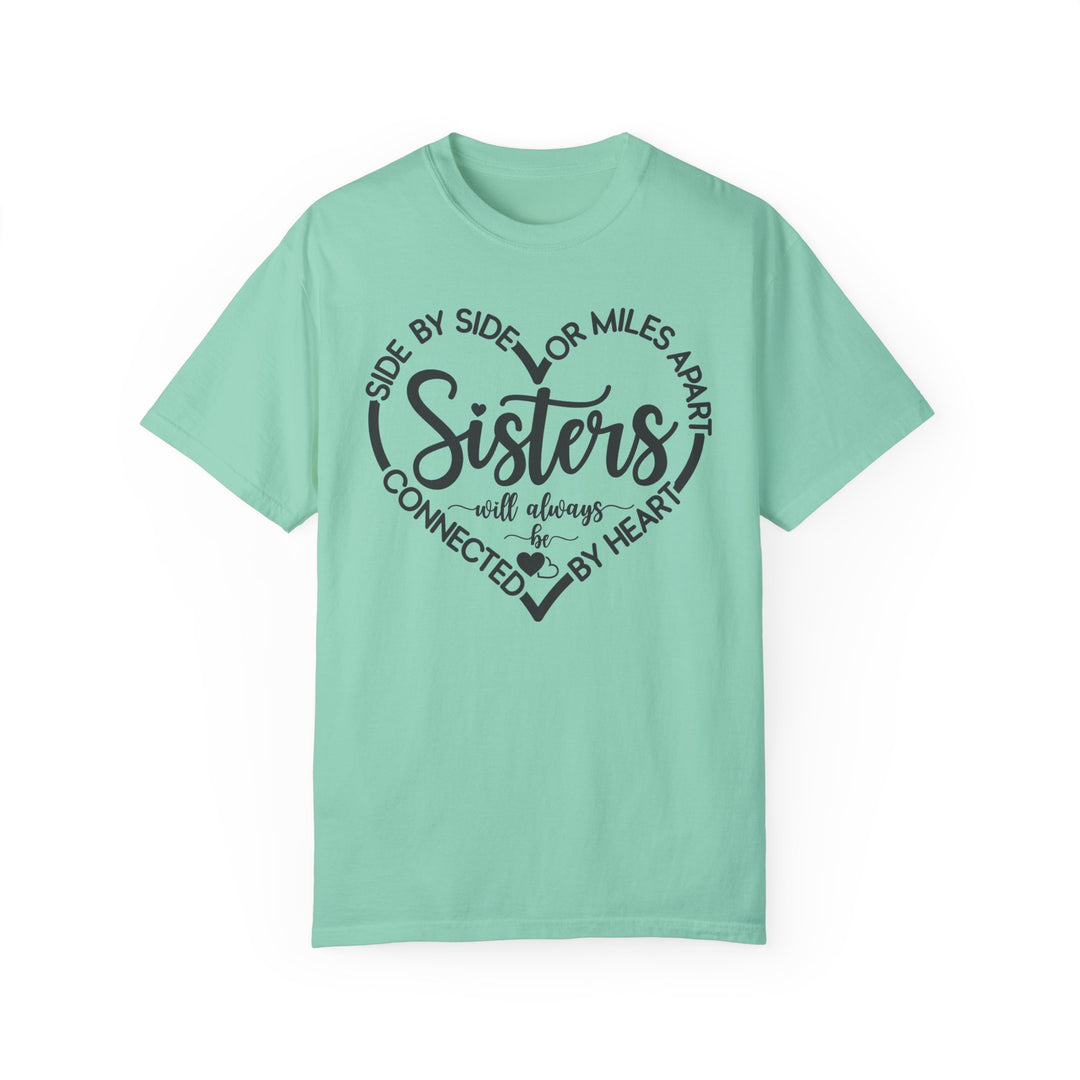 Sisters At Heart Tee featuring black text and heart design on a green, 100% ring-spun cotton t-shirt, offering a cozy, relaxed fit.