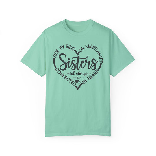 Sisters At Heart Tee featuring black text and heart design on a green, 100% ring-spun cotton t-shirt, offering a cozy, relaxed fit.