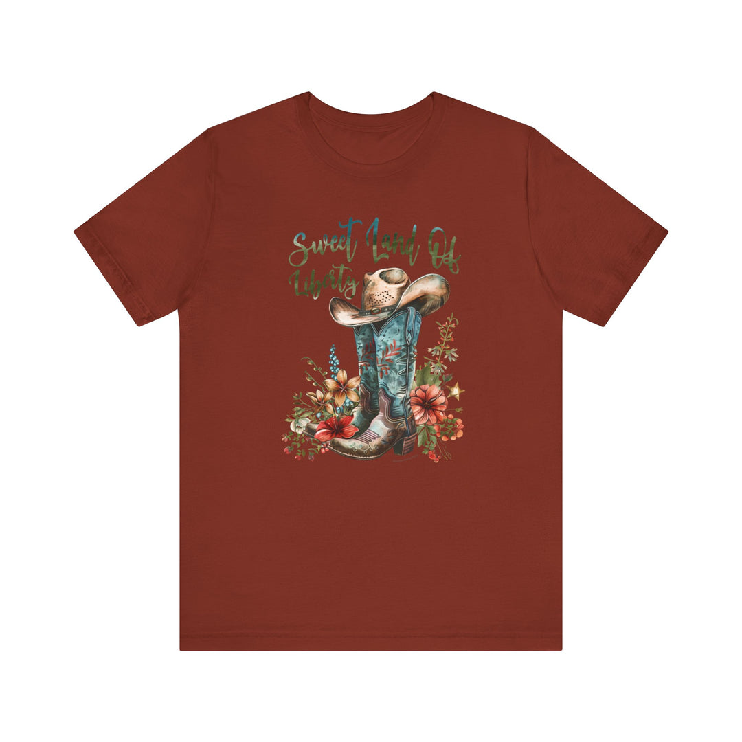 A red shirt featuring a cowboy hat and flowers, embodying a classic Americana vibe. Unisex jersey tee with ribbed knit collars, taping on shoulders, and 100% Airlume combed cotton for comfort. Sweet Land of Liberty Tee by Worlds Worst Tees.