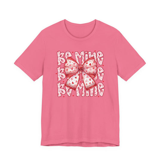 Be Mine Tee with heart-spattered bow and BE MINE text, perfect for Valentine's Day. Classic unisex fit, soft cotton, ribbed collar, and durable stitching.