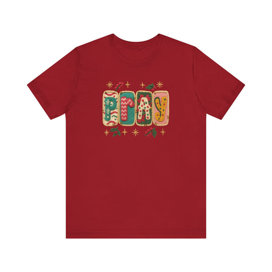 Unisex Pray Tee with a holiday-themed PLAY graphic, featuring knitted pillow-style letters and festive motifs, on a soft cotton red T-shirt.