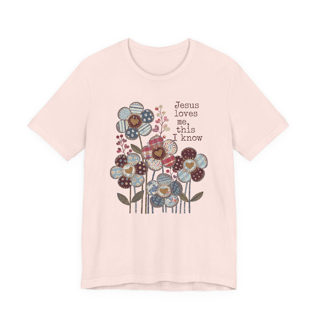 Jesus Loves Me Tee featuring patchwork flowers with heart centers and typewriter text. Soft cotton, unisex fit, ribbed knit collar, dual side seams for durability.