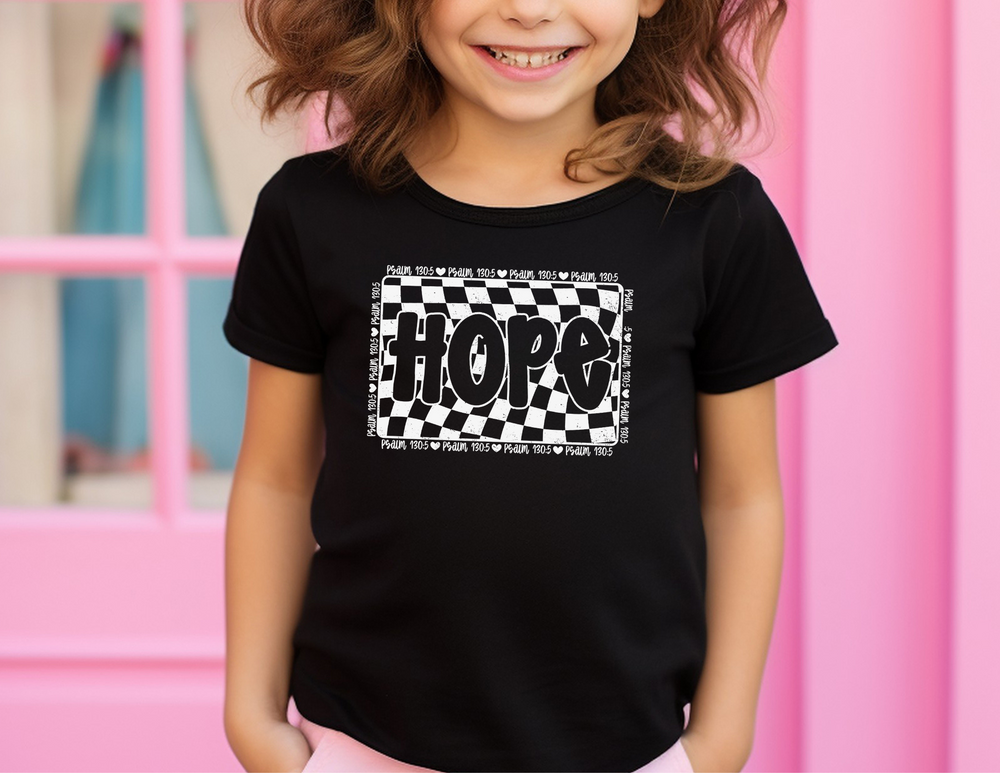 Girl wearing the Hope Toddler Tee, a comfortable Bella Canvas short sleeve t-shirt, smiling at the camera with a checkered background.