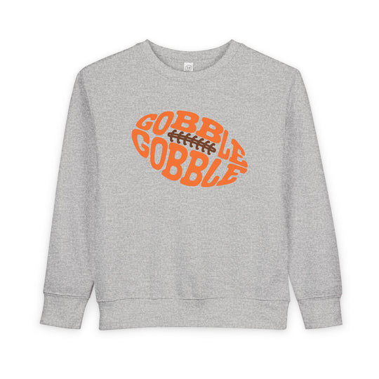 Heather-gray toddler sweatshirt with a football-shaped graphic saying “GOBBLE GOBBLE” in orange, blending warmth and playful Thanksgiving style.