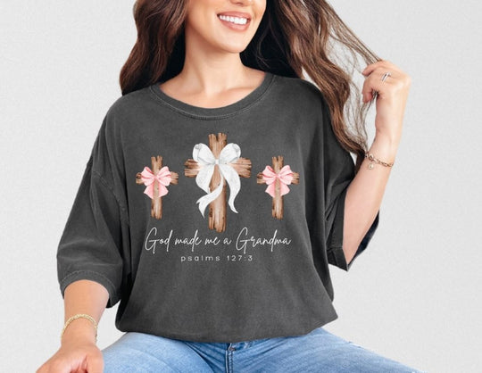 Woman wearing God Made Me a Grandma tee with rustic wooden cross design, paired with light jeans and jewelry, showcasing a relaxed fit from Faith Family Designs.