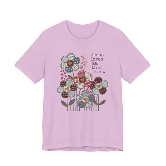 Light pink T-shirt featuring whimsical patchwork flowers and Jesus loves me, this I know text, offering a soft, comfortable fit from Faith Family Designs.
