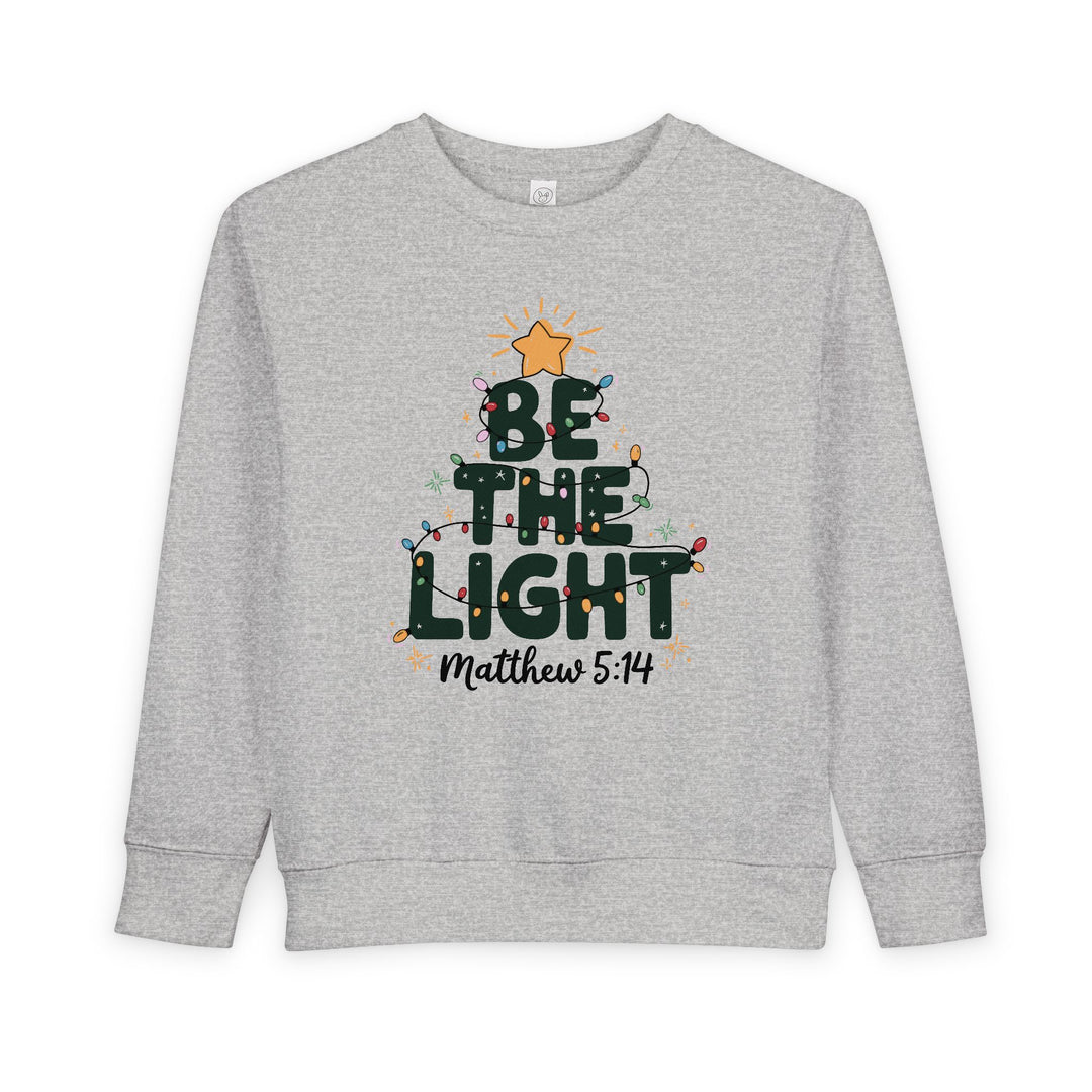 Be the Light Toddler Crew: Light-gray sweatshirt with a festive tree graphic, BE THE LIGHT text, colorful lights, gold star, and Matthew 5:14 reference.