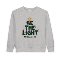 Be the Light Toddler Crew: Light-gray sweatshirt with a festive tree graphic, BE THE LIGHT text, colorful lights, gold star, and Matthew 5:14 reference.