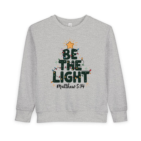 Be the Light Toddler Crew: Light-gray sweatshirt with a festive tree graphic, BE THE LIGHT text, colorful lights, gold star, and Matthew 5:14 reference.