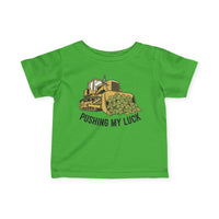 Pushing My Luck Baby Tee featuring a yellow bulldozer with shamrocks, slogan below, designed for toddlers with durable, soft cotton material and classic fit.