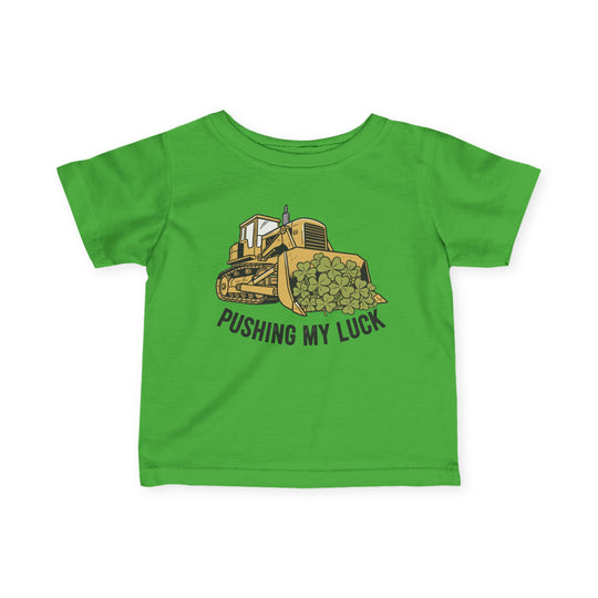 Pushing My Luck Baby Tee featuring a yellow bulldozer with shamrocks, slogan below, designed for toddlers with durable, soft cotton material and classic fit.