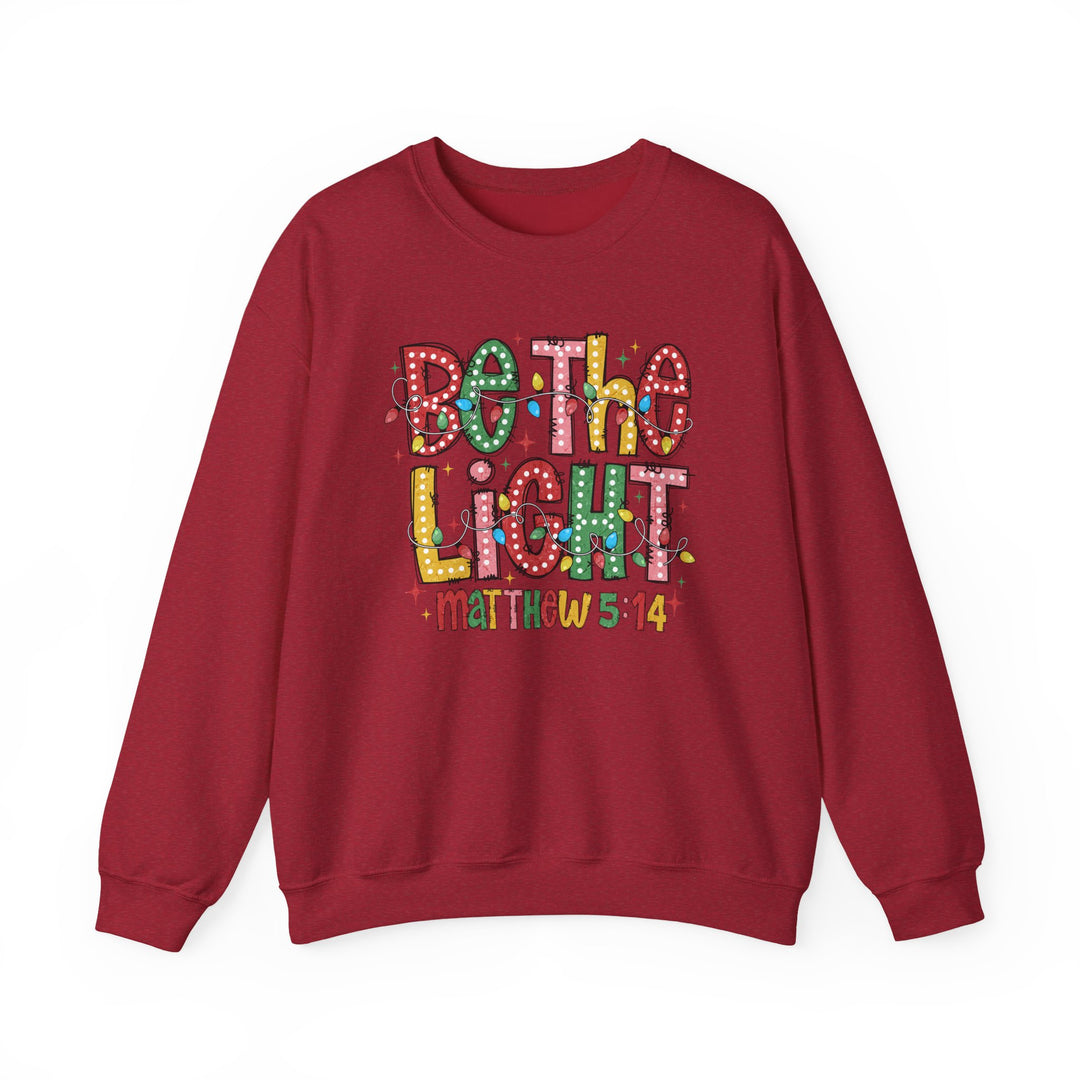 Be the Light Crew sweatshirt features a playful Christmas graphic with colorful lights and 'Matthew 5:14' on a cozy, durable fabric blend.