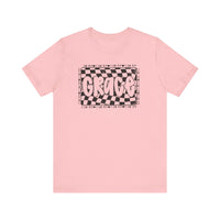 Grace Tee: A pink t-shirt featuring bold black and white text, crafted from soft cotton for a classic unisex fit with ribbed collars and durable seams.