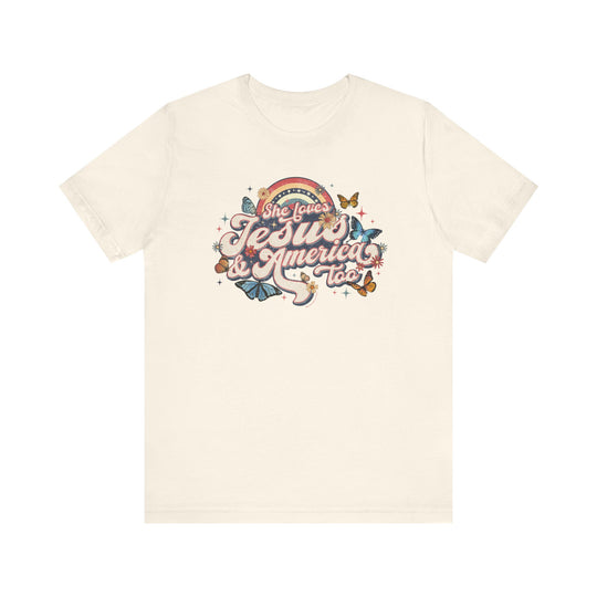 A white t-shirt featuring a graphic design of butterflies and flowers, titled She Loves Jesus and America Tee. Unisex jersey tee with ribbed knit collars, taping on shoulders, and tear-away label. 100% Airlume combed cotton, retail fit.