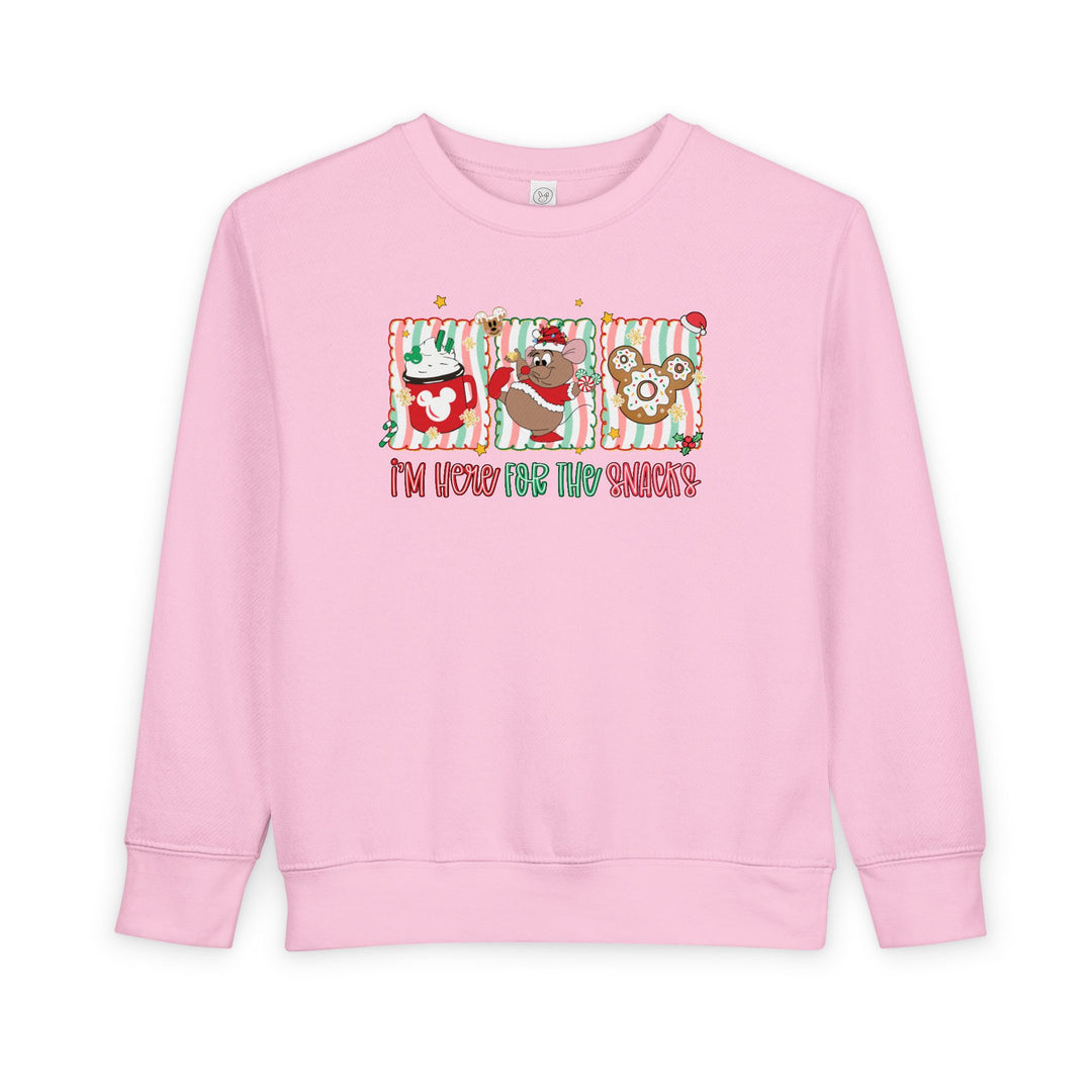 Light-pink toddler crewneck sweatshirt with Christmas-themed graphics: hot cocoa, cartoon mouse with Santa hat, Mickey gingerbread cookie, and slogan “I’m here for the snacks!”.
