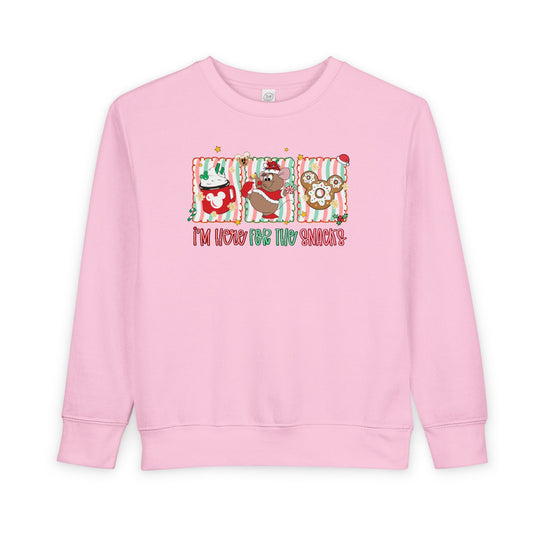 Light-pink toddler crewneck sweatshirt with Christmas-themed graphics: hot cocoa, cartoon mouse with Santa hat, Mickey gingerbread cookie, and slogan “I’m here for the snacks!”.