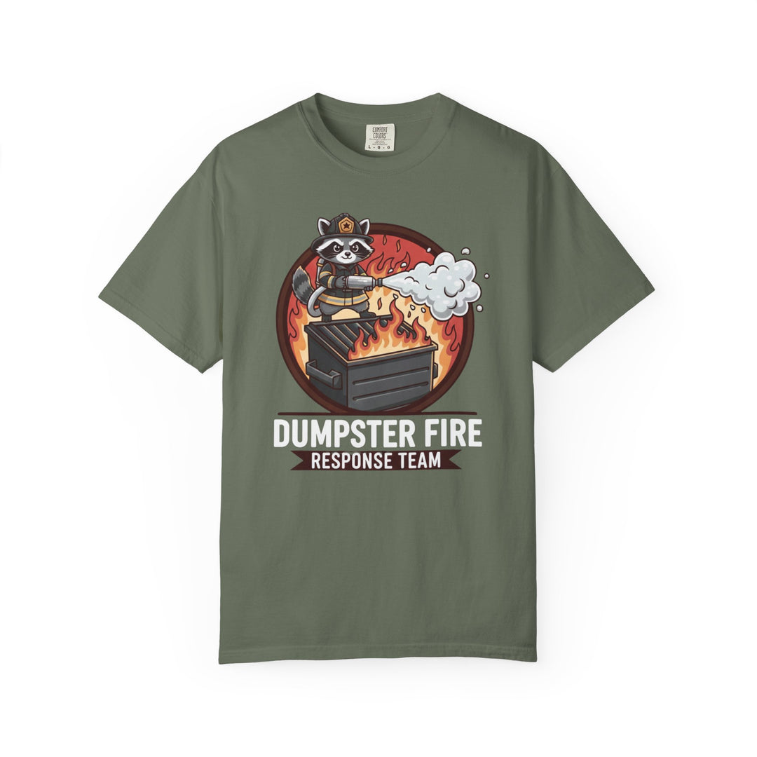 Olive-green T-shirt featuring a cartoon raccoon firefighter spraying foam on a dumpster, captioned “DUMPSTER FIRE RESPONSE TEAM,” highlighting unique graphic appeal from Faith Family Designs.