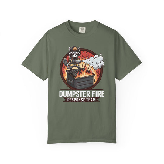 Olive-green T-shirt featuring a cartoon raccoon firefighter spraying foam on a dumpster, captioned “DUMPSTER FIRE RESPONSE TEAM,” highlighting unique graphic appeal from Faith Family Designs.