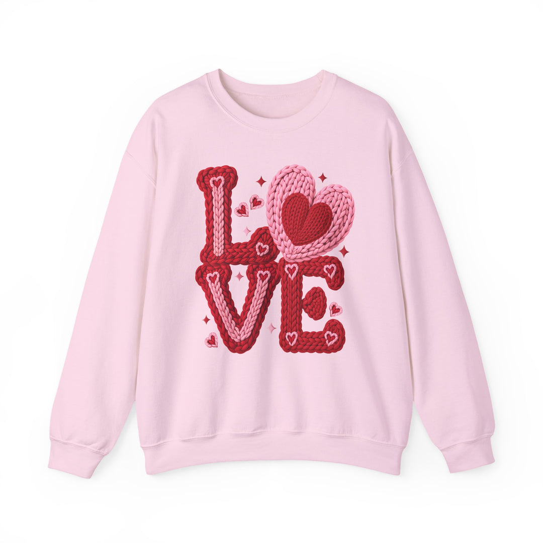 Light pink crewneck sweatshirt reading LOVE in chunky knit-style letters with heart and sparkle motifs, embodying a cozy, Valentine-themed design.