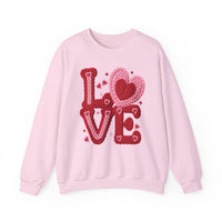 Light pink crewneck sweatshirt reading LOVE in chunky knit-style letters with heart and sparkle motifs, embodying a cozy, Valentine-themed design.