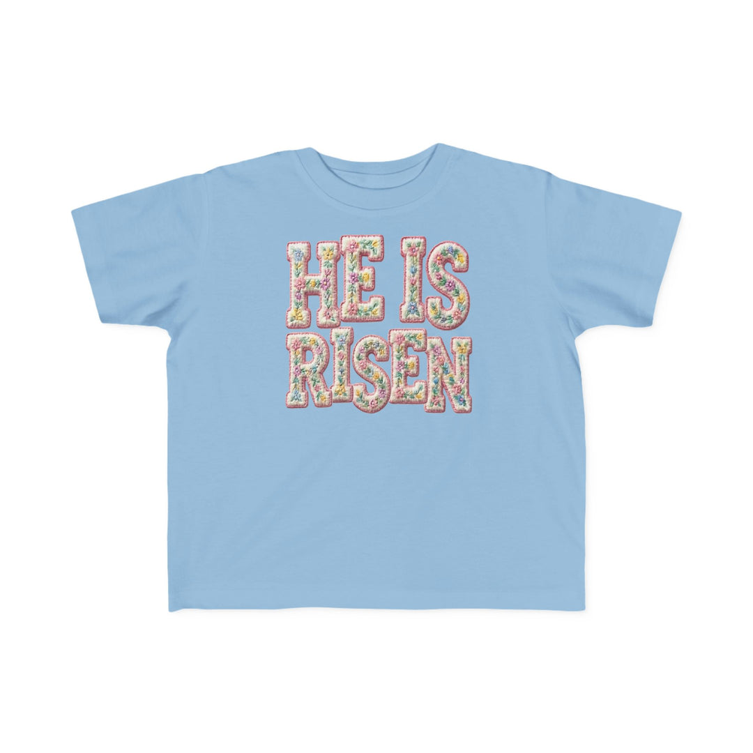 He is Risen Toddler Tee: Light-blue, short-sleeve shirt featuring HE IS RISEN in pastel floral pattern, crafted for toddlers with soft, durable cotton; perfect for sensitive skin.
