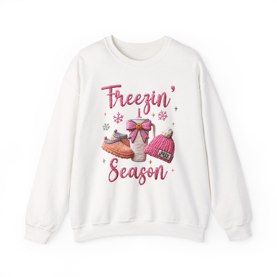 Freezin Season Crew: White crew-neck sweatshirt featuring winter-themed graphics with a steaming mug, slippers, beanie, and snowflakes, perfect for cozy comfort.